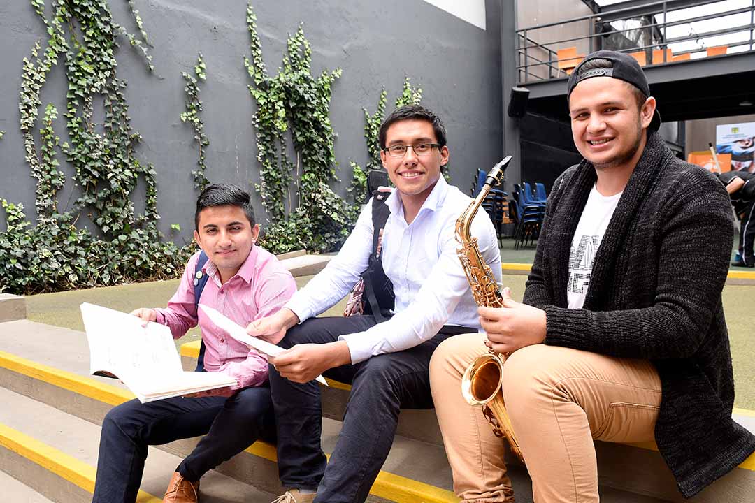 Imagen de tres beneficiarios del ICETEX con libros e instrumentos musicales