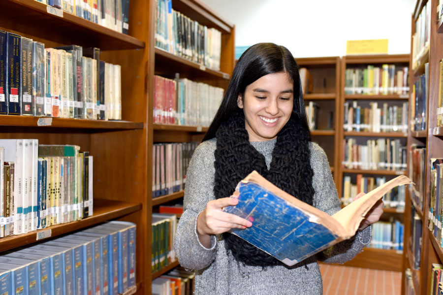 Foto de estudiante en una biblioteca leyendo un libro
