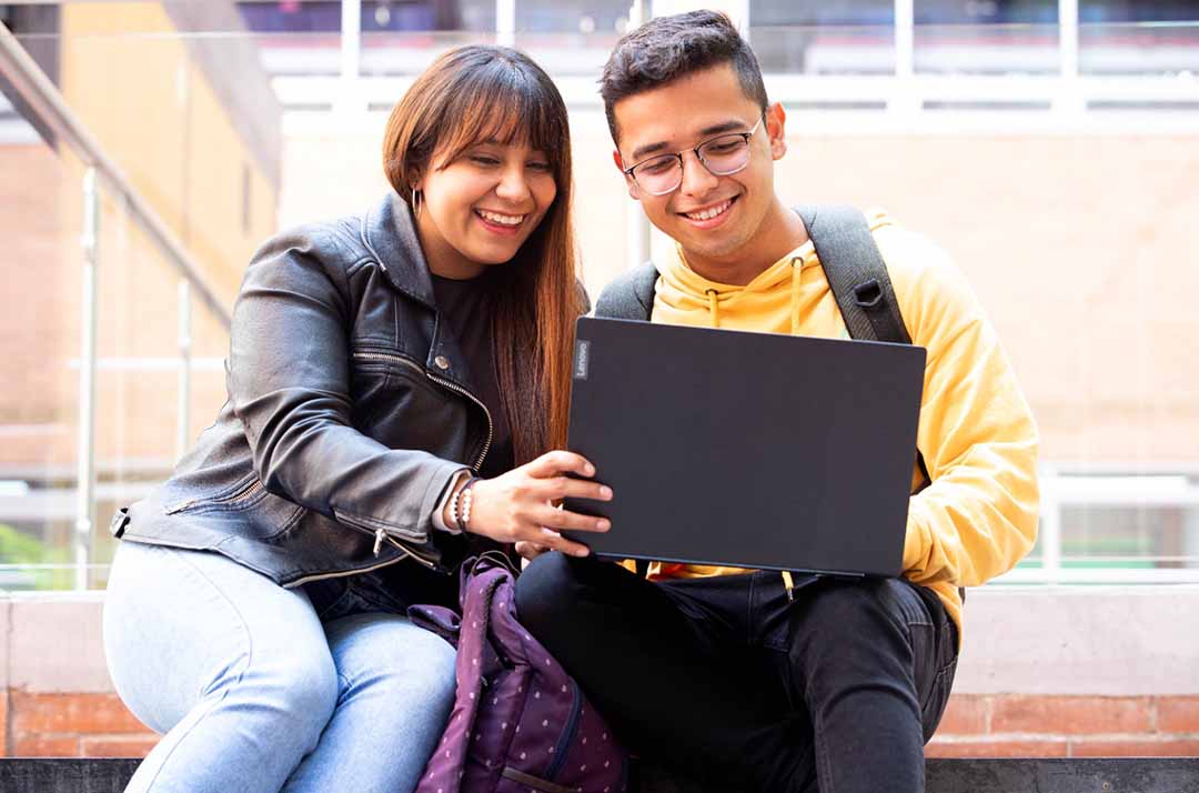 Imagen de estudiantes de universidad sentados en un corredor usando un computador