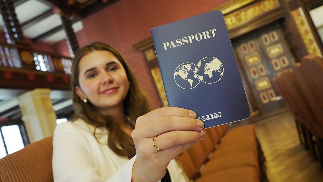 Imagen de una mujer sentada sonriendo mostrando el pasaporte de ICETEX