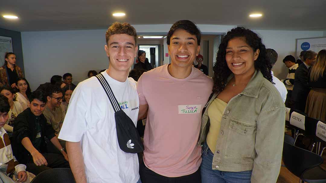 Imagen de tres estudiantes de universidad abrazados sonriendo en un evento de ICETEX