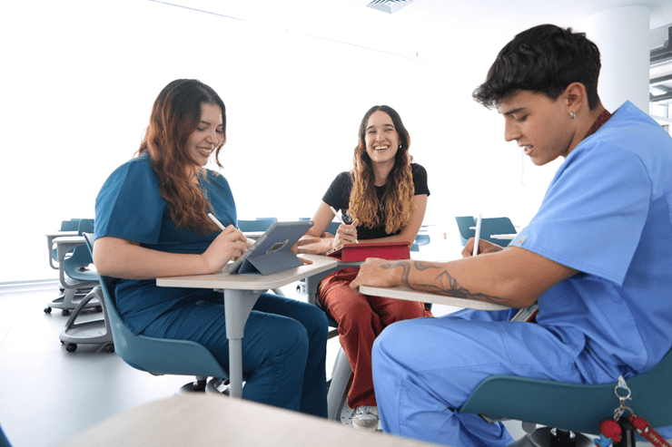 Imagen de tres estudiantes de universidad sonriendo mientras estudian sentados